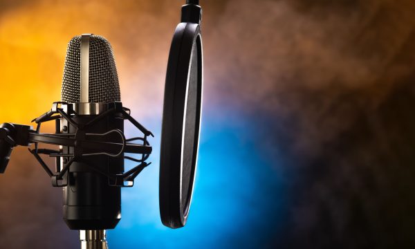 Professional studio microphone and pop filter on a beautiful yel Professional studio microphone and pop filter on a beautiful yellow-blue smoky background. Night club, concert, radio broadcasting, television, recording studio, purity of sound, vocals, music.