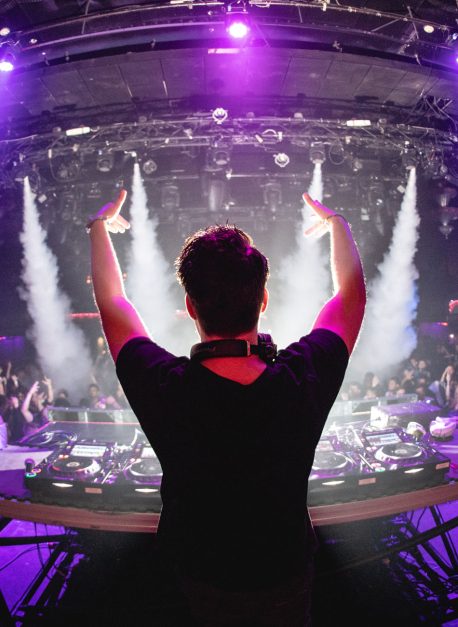 DJ in nightclub with hands up and cryo canons, shot from behind Photo by andrewmacrobert.com