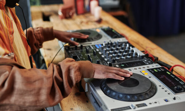 Hands of black man creating new music and recording it for entertainment event Hands of black man in casualwear standing by wooden table and creating new music and recording it for entertainment event